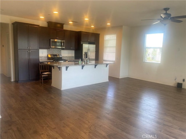 kitchen featuring dark wood-style floors, a kitchen bar, a kitchen island with sink, and appliances with stainless steel finishes