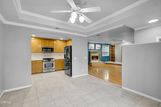 kitchen with a raised ceiling, ceiling fan, a fireplace, and stainless steel appliances