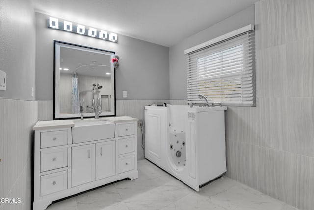 bathroom featuring a washtub, vanity, and tile walls