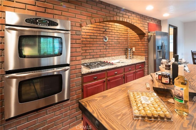 kitchen featuring stainless steel appliances, brick wall, and wood counters