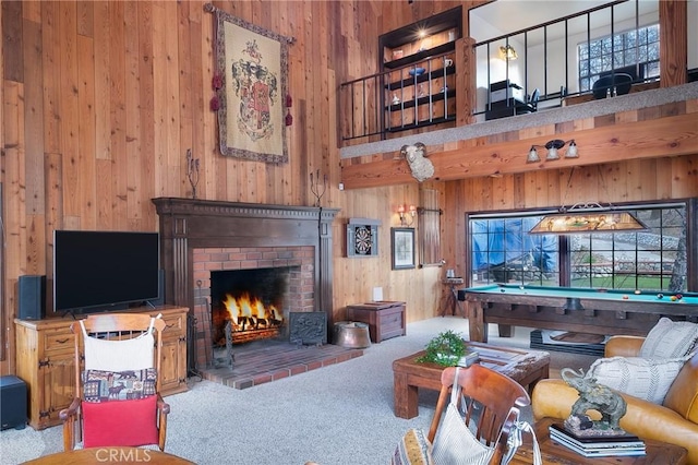 carpeted living room with wooden walls, a towering ceiling, billiards, and a brick fireplace