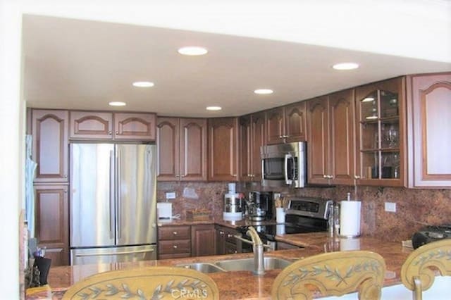 kitchen featuring decorative backsplash, glass insert cabinets, a peninsula, stainless steel appliances, and a sink