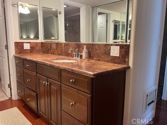 bathroom featuring visible vents, wood finished floors, vanity, and decorative backsplash