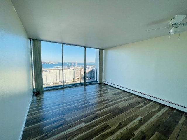 empty room featuring baseboard heating, a water view, dark hardwood / wood-style floors, and a wall of windows