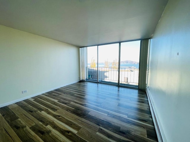 spare room with baseboard heating, a wall of windows, dark hardwood / wood-style flooring, and a water view