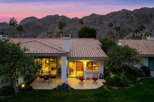 back house at dusk with a lawn, a mountain view, and a patio