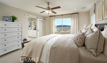 carpeted bedroom with ceiling fan, a barn door, and connected bathroom