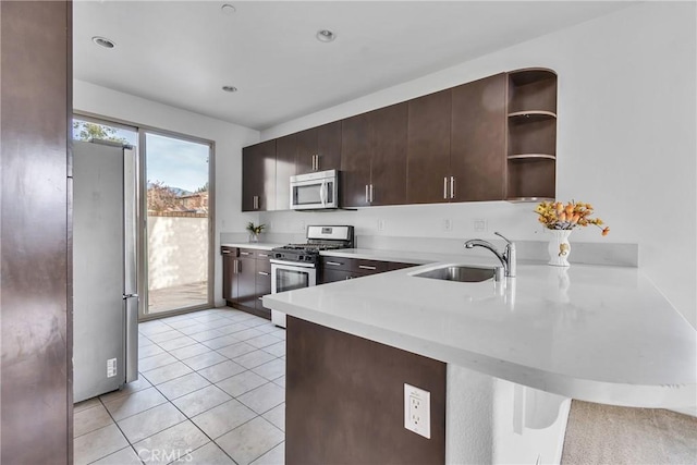 kitchen featuring kitchen peninsula, dark brown cabinetry, stainless steel appliances, sink, and light tile patterned floors