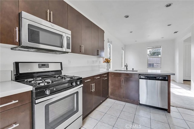 kitchen with kitchen peninsula, sink, appliances with stainless steel finishes, light tile patterned flooring, and dark brown cabinetry