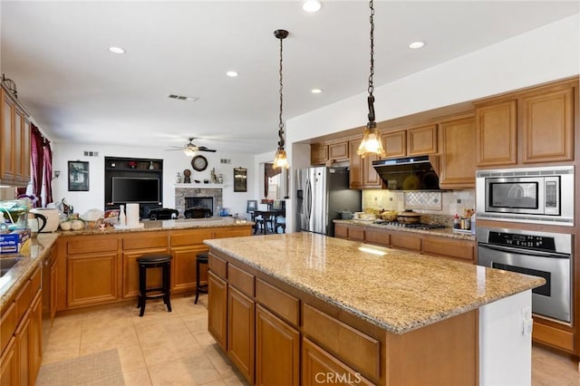 kitchen with a center island, ceiling fan, light tile patterned floors, light stone countertops, and appliances with stainless steel finishes