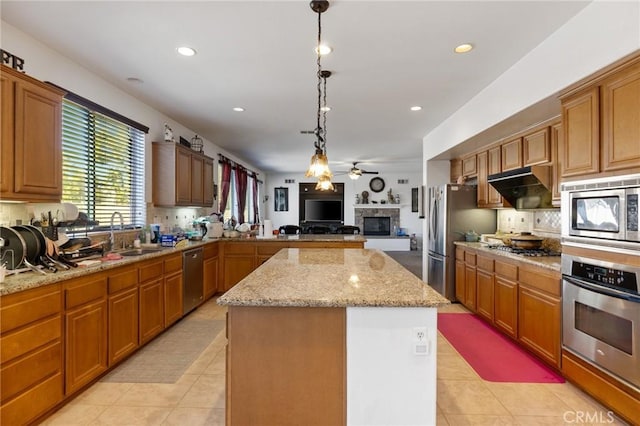 kitchen featuring sink, stainless steel appliances, light tile patterned floors, a stone fireplace, and a kitchen island