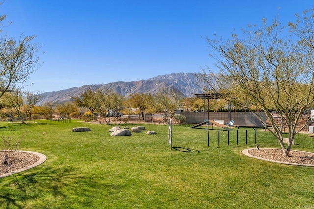 view of home's community with a mountain view, a lawn, and fence