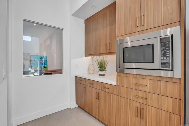 kitchen with light countertops, stainless steel microwave, concrete floors, and baseboards