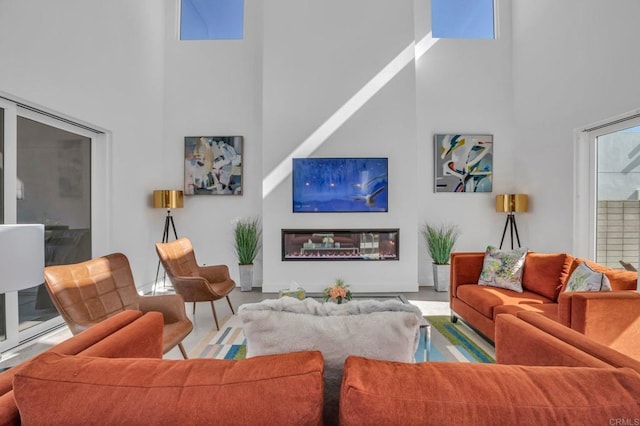 living area with a wealth of natural light, a glass covered fireplace, and a towering ceiling