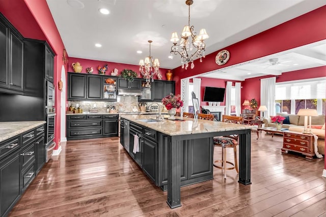 kitchen featuring sink, decorative light fixtures, a kitchen island with sink, and dark hardwood / wood-style floors