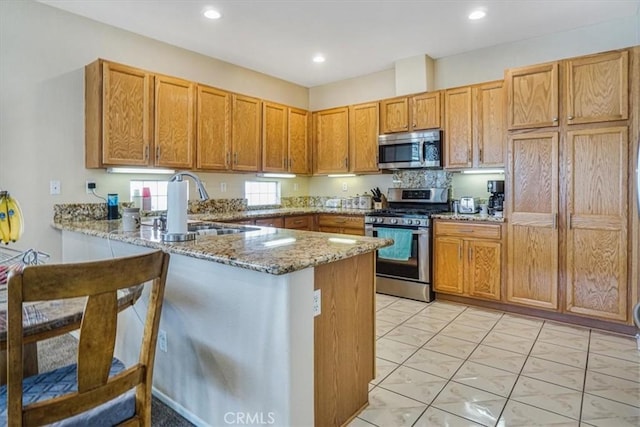 kitchen featuring kitchen peninsula, light stone countertops, sink, and stainless steel appliances