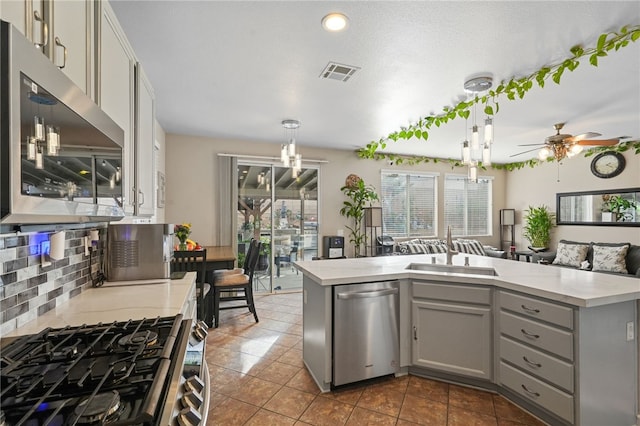 kitchen with gray cabinetry, sink, stainless steel appliances, decorative light fixtures, and decorative backsplash