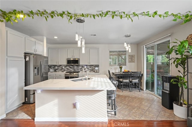 kitchen featuring appliances with stainless steel finishes, a kitchen island with sink, hanging light fixtures, and sink