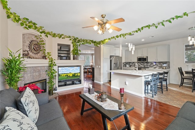 living room featuring a tile fireplace, ceiling fan, dark hardwood / wood-style flooring, and sink