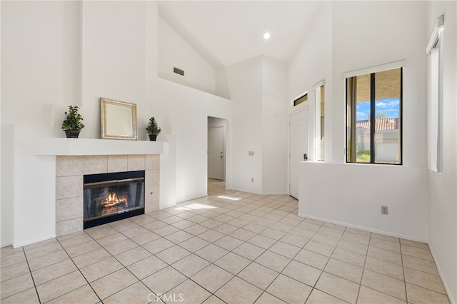 unfurnished living room featuring baseboards, high vaulted ceiling, a tiled fireplace, and visible vents