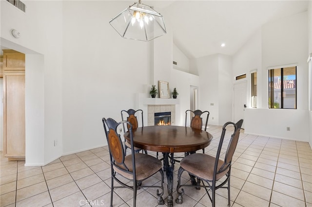 dining space with a tile fireplace, light tile patterned floors, visible vents, and high vaulted ceiling