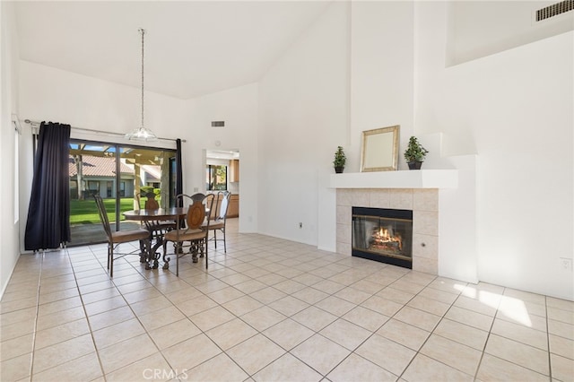 dining area featuring a tile fireplace, light tile patterned floors, a high ceiling, and visible vents