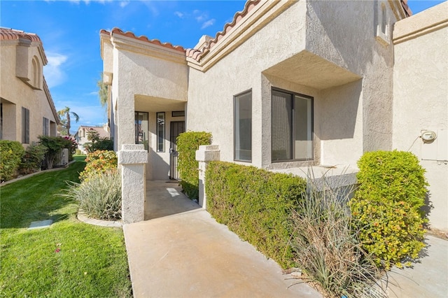 doorway to property with a yard, stucco siding, and a tile roof