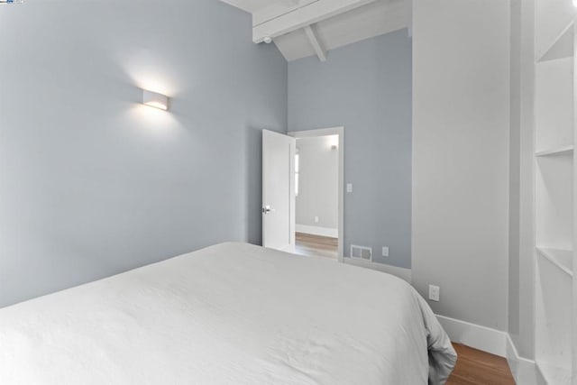 bedroom with lofted ceiling with beams and wood-type flooring