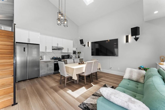 dining area featuring a chandelier, high vaulted ceiling, and light hardwood / wood-style flooring