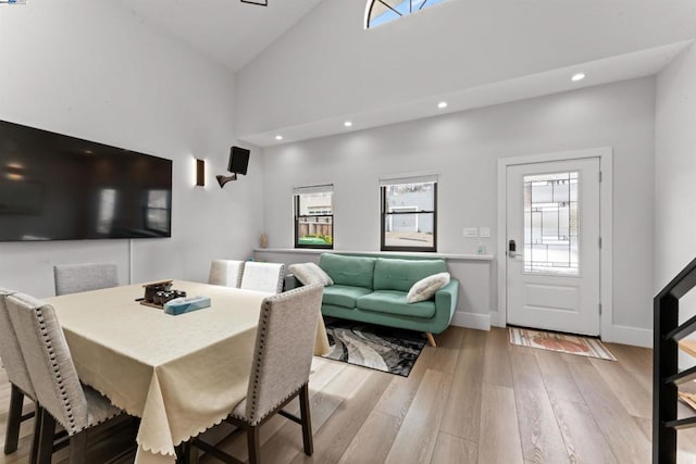 dining area with high vaulted ceiling and light hardwood / wood-style floors