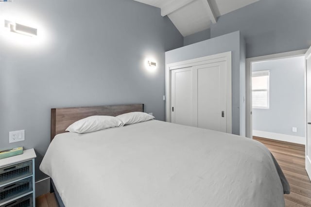 bedroom with a closet, lofted ceiling with beams, and hardwood / wood-style flooring