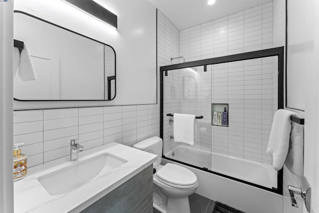 full bathroom with vanity, backsplash, bath / shower combo with glass door, toilet, and tile walls