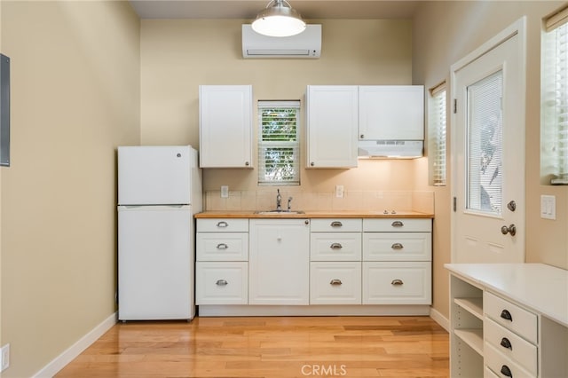 kitchen featuring sink, white cabinetry, decorative light fixtures, an AC wall unit, and white refrigerator