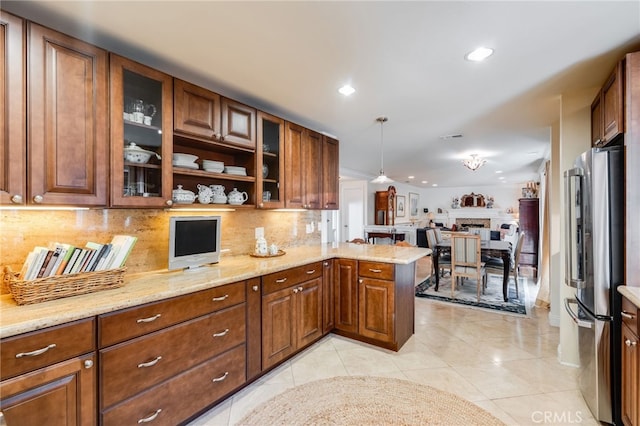 kitchen featuring decorative light fixtures, light tile patterned floors, stainless steel refrigerator, kitchen peninsula, and light stone countertops