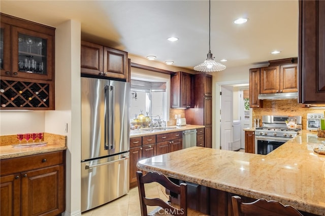 kitchen featuring pendant lighting, sink, a kitchen bar, light stone counters, and stainless steel appliances