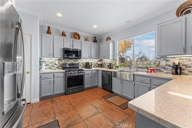 kitchen featuring decorative backsplash, appliances with stainless steel finishes, gray cabinets, crown molding, and a sink