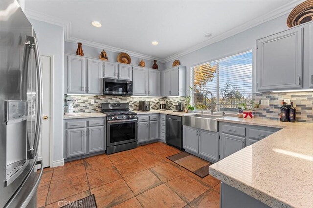 kitchen with appliances with stainless steel finishes, ornamental molding, backsplash, a sink, and gray cabinetry