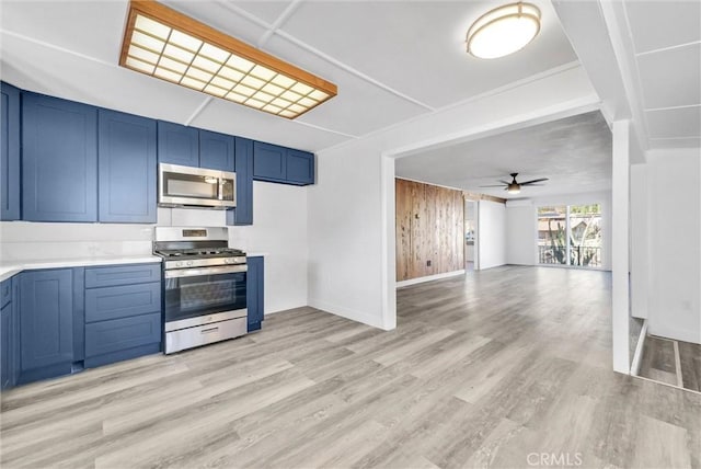 kitchen featuring ceiling fan, stainless steel appliances, blue cabinets, wood walls, and light hardwood / wood-style floors