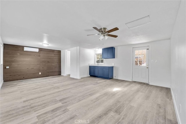 unfurnished living room with a wall mounted air conditioner, ceiling fan, light wood-type flooring, and wooden walls