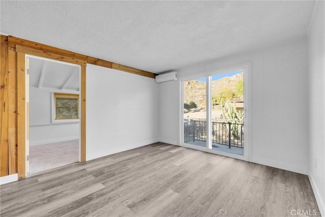 unfurnished room featuring a textured ceiling, a wall mounted AC, light hardwood / wood-style flooring, and lofted ceiling