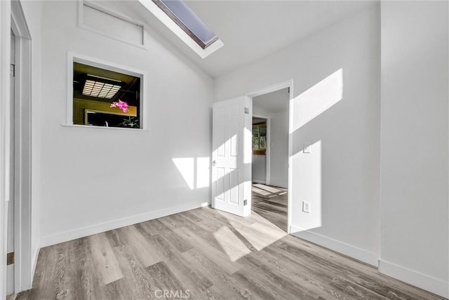 empty room with vaulted ceiling with skylight and light hardwood / wood-style floors