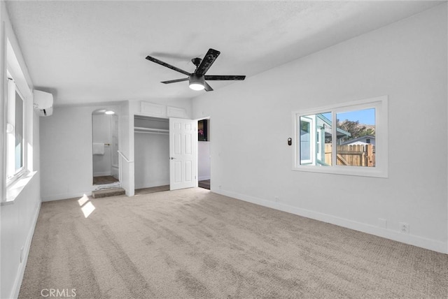 unfurnished bedroom featuring light carpet, connected bathroom, a wall unit AC, and ceiling fan