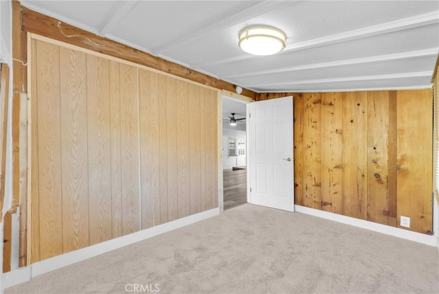 empty room featuring carpet flooring, ceiling fan, and wood walls