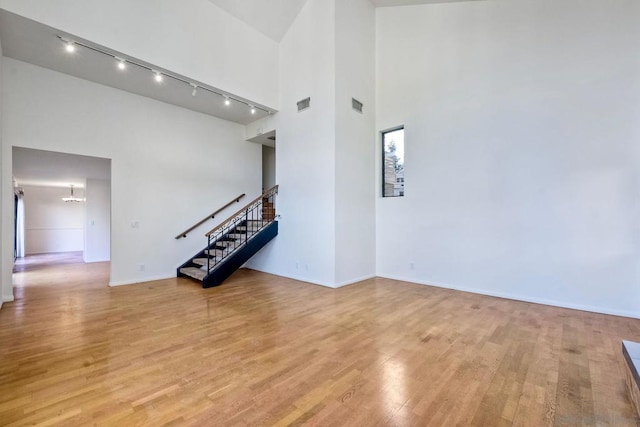 unfurnished living room with an inviting chandelier, light hardwood / wood-style flooring, and a high ceiling