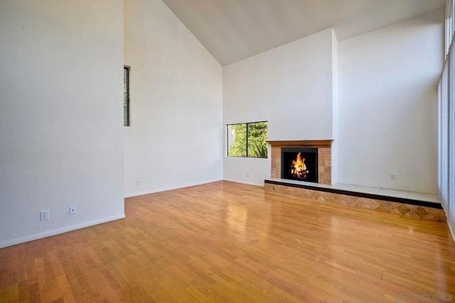 unfurnished living room featuring high vaulted ceiling, a tile fireplace, and light wood-type flooring