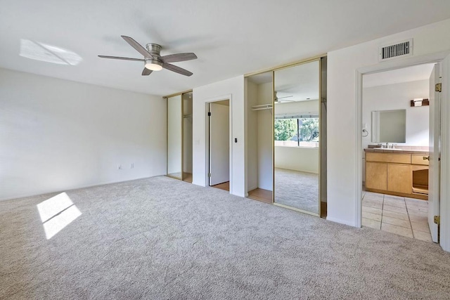 unfurnished bedroom with ceiling fan, light colored carpet, sink, and ensuite bath