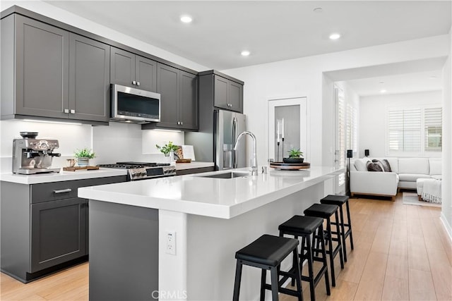 kitchen with light hardwood / wood-style floors, a breakfast bar, stainless steel appliances, a kitchen island with sink, and gray cabinets