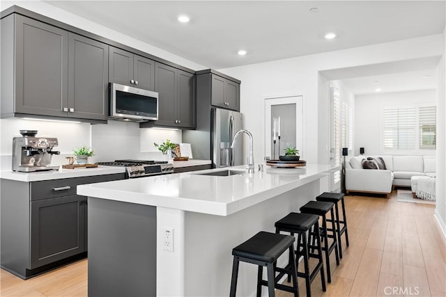 kitchen featuring sink, gray cabinetry, a kitchen breakfast bar, an island with sink, and stainless steel appliances