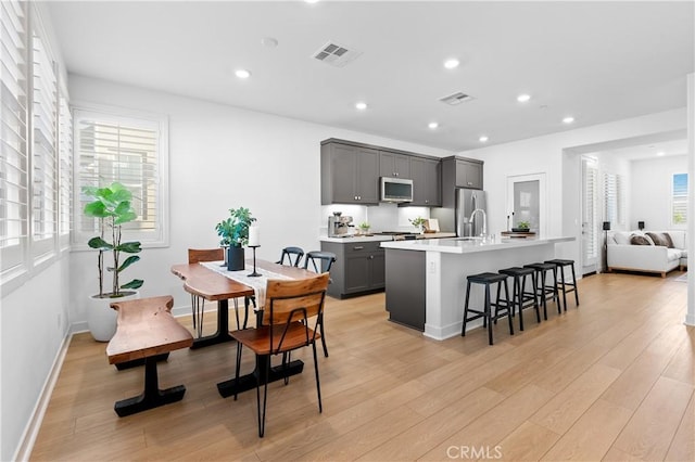 kitchen with a center island with sink, a kitchen breakfast bar, gray cabinets, stainless steel appliances, and light hardwood / wood-style floors