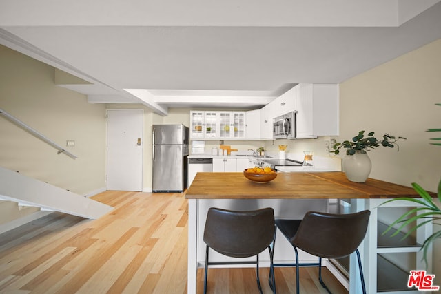 kitchen with a kitchen breakfast bar, light hardwood / wood-style flooring, kitchen peninsula, white cabinets, and appliances with stainless steel finishes